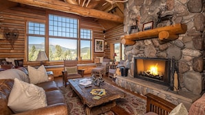 A log cabin interior with a stone fireplace, large windows, and rustic furnishings. - Enchanting Private Mountain Sanctuary! Spectacular Views (Big Sky)