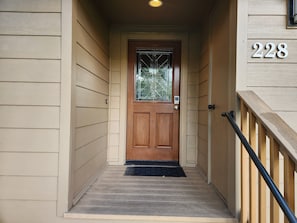 A wooden door with a glass panel, a black doormat, and a number '228' on the wall.