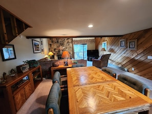 A cozy living room with a wooden herringbone dining table, comfortable seating, a fireplace, and a stone accent wall.