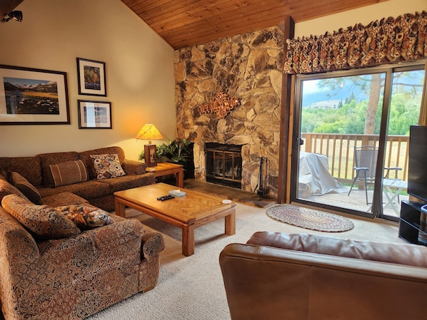 A cozy living room with a stone fireplace, a sofa, a coffee table, and a TV.