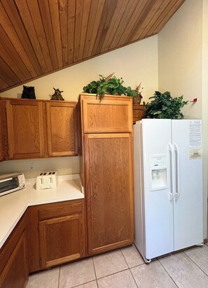 A kitchen with wooden cabinets, a white refrigerator, a toaster, and a potted plant on the counter.