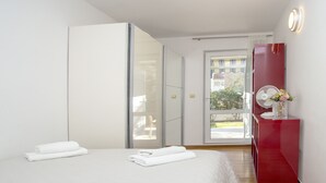A hotel room with a bed, a red dresser, a mirror, and a window with a view of buildings and trees. - Deluxe apartment Lea with large garden (Split)