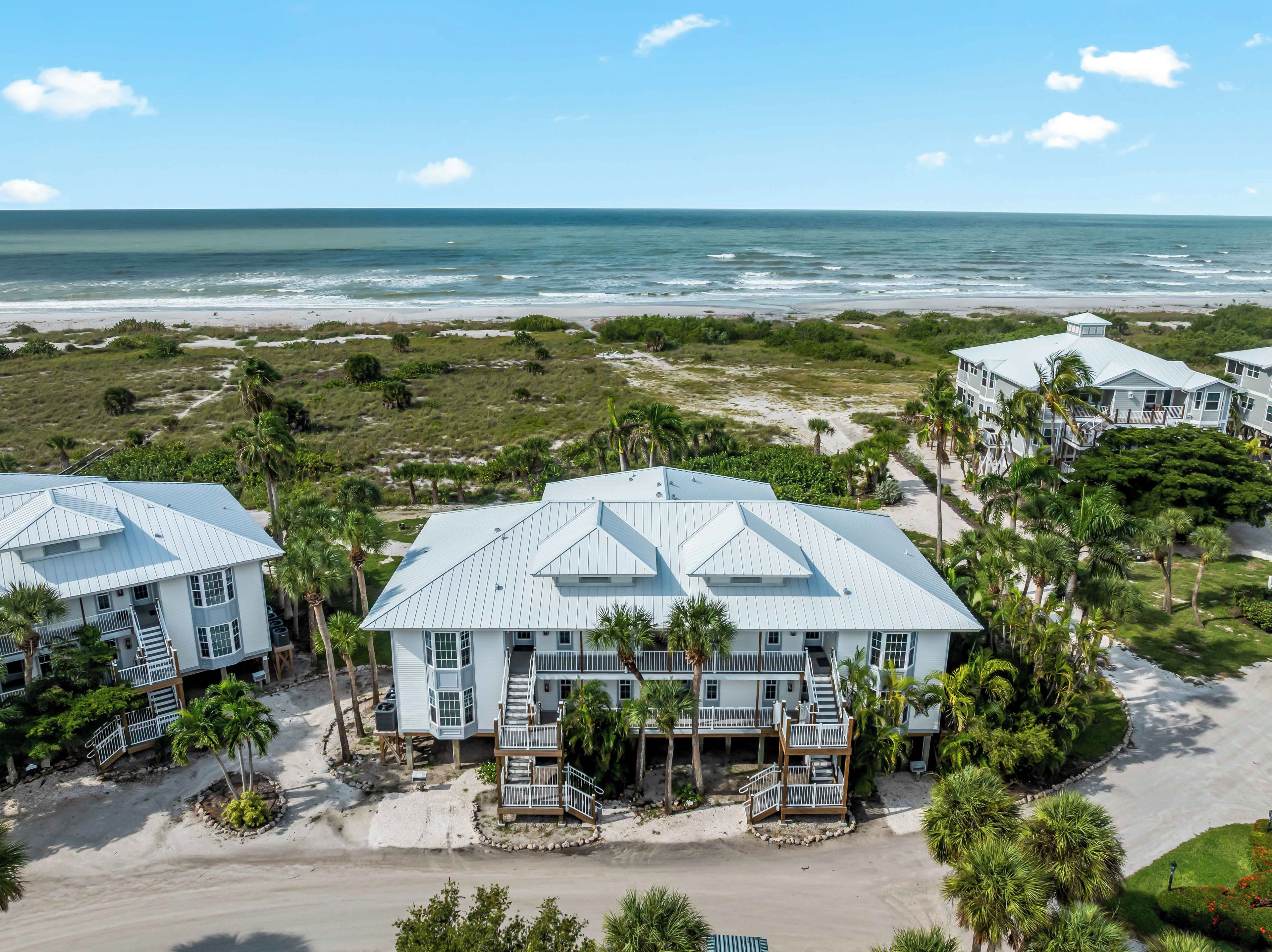 A beachfront property with multiple buildings, including a prominent house with a large balcony and a smaller structure to the left.