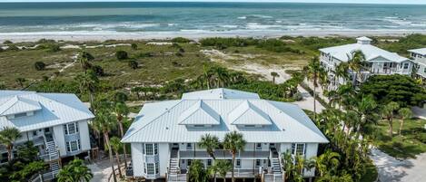 A beachfront property with multiple buildings, including a prominent house with a large balcony and a smaller structure to the left.