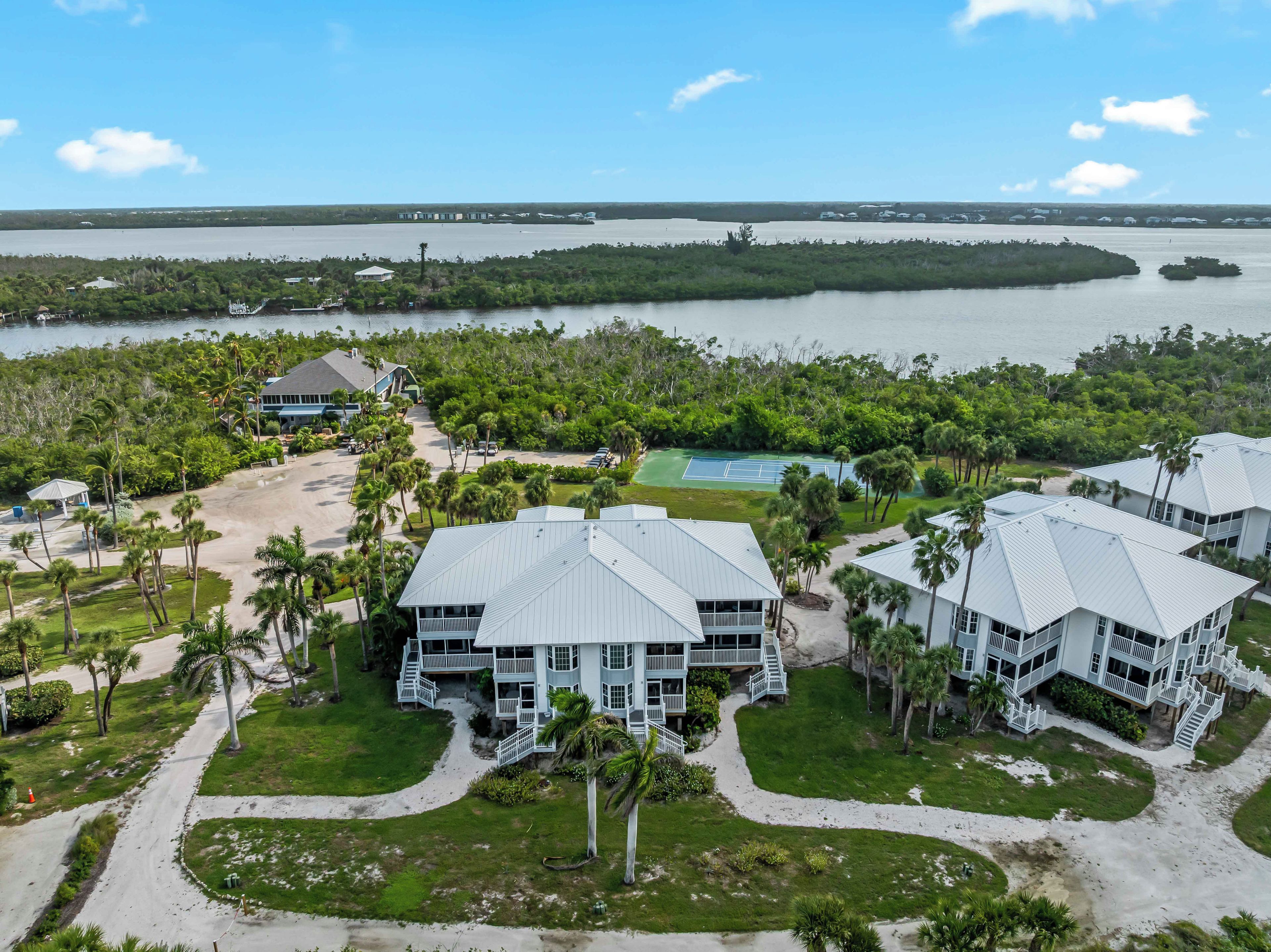 A resort with multiple buildings, a tennis court, and a view of the water.