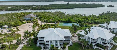 A resort with multiple buildings, a tennis court, and a view of the water.