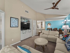 A living room with a television, sofa, ottoman, and a ceiling fan.