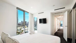 A hotel room with a large bed, a TV mounted on the wall, and a view of the cityscape through large windows. - H Residences Level 10, Ocean, Free Wi-Fi, Parking, Foxtel (Gold Coast)