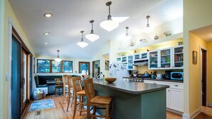 A modern kitchen with a central island, wooden chairs, and a view of the outdoors through large windows. - PRIVATE HEATED POOL and PET FRIENDLY! (3 Nt Min!) (Michiana Shores)