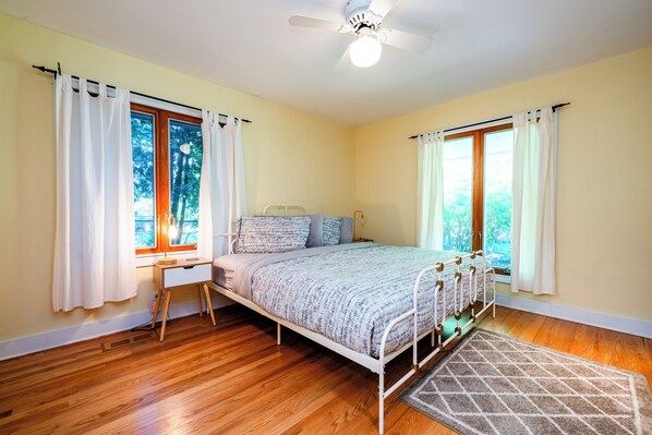 A bedroom with a bed, bedside table, lamp, and a view of trees through the windows. - PRIVATE HEATED POOL and PET FRIENDLY! (3 Nt Min!) (Michiana Shores)