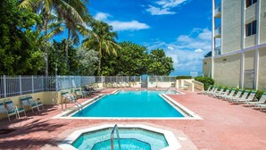 A swimming pool with lounge chairs, a hot tub, and a fenced area with palm trees. - Magnificent beachfront condo w/ pool & parking at Apollo Condominium (Marco Island)