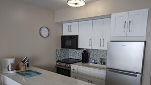 A modern kitchen with white cabinets, a stainless steel refrigerator, a coffee maker, and a clock on the wall. - Magnificent beachfront condo w/ pool & parking at Apollo Condominium (Marco Island)