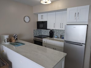 Una cocina moderna con armarios blancos, un refrigerador de acero inoxidable, una cafetera y un reloj en la pared.