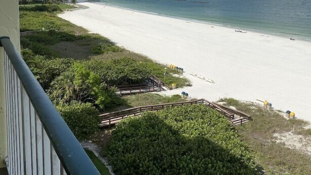A beach view with a clear sky, a sandy beach, and a building in the background. - Magnificent beachfront condo w/ pool & parking at Apollo Condominium (Marco Island)
