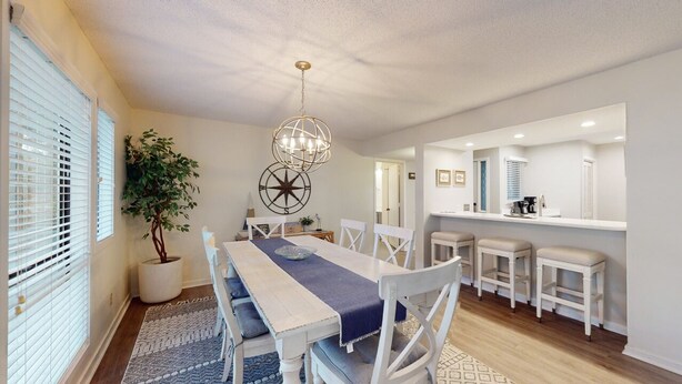 Un espace repas avec une longue table, des chaises blanches, un lustre et une plante en pot.