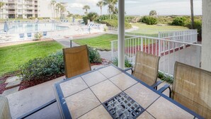 A balcony with a view of a swimming pool, a grassy area, and a building with multiple balconies. - CRC 1104 - Gorgeous Pool Front Ground Floor Condo (St Augustine)