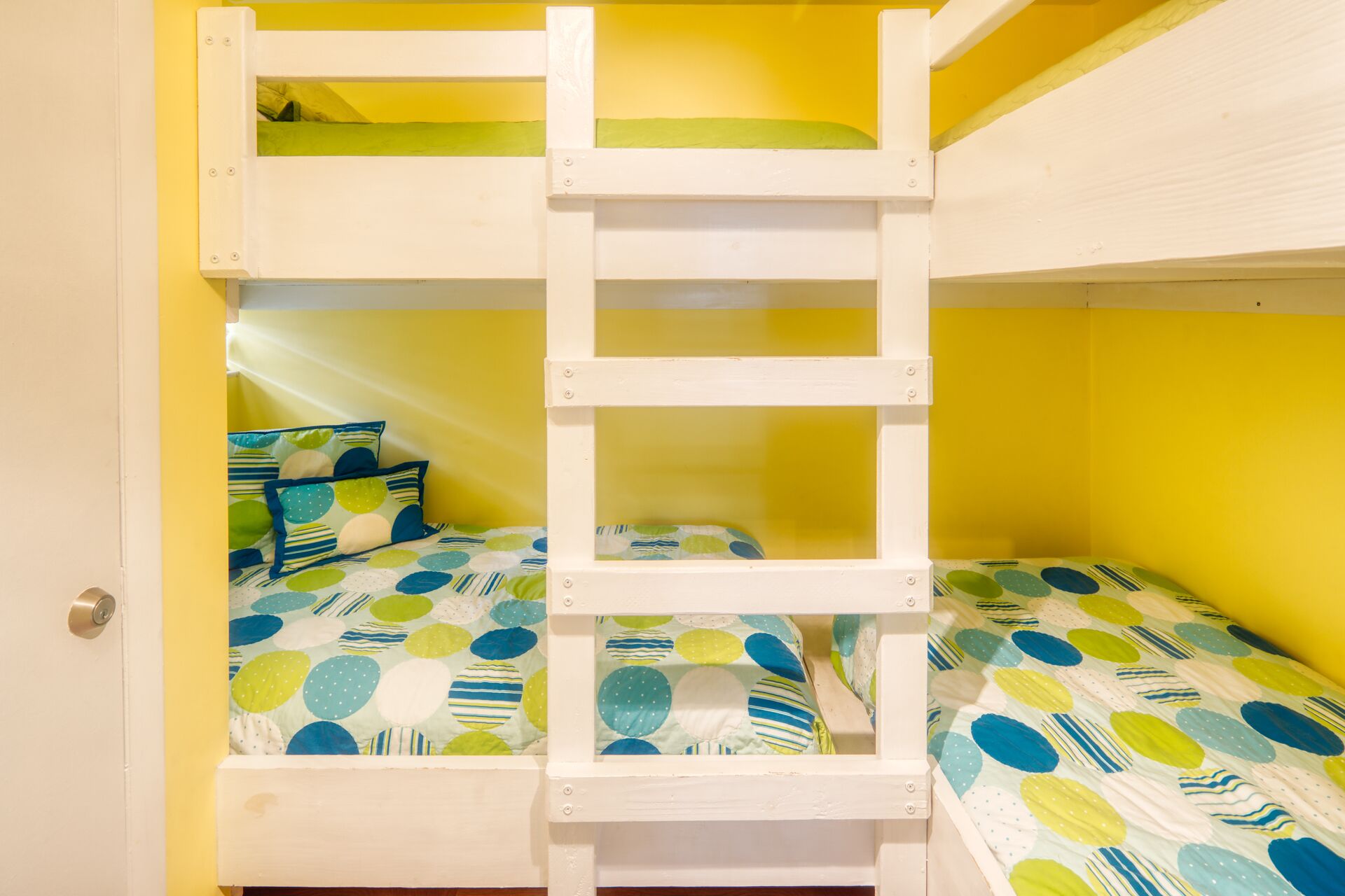 A bunk bed with a polka dot bedspread and pillows, in a room with yellow walls.