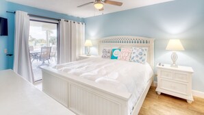 A bedroom with a bed, two bedside tables, a ceiling fan, and a view of the outdoors. - CRC 1104 - Gorgeous Pool Front Ground Floor Condo (St Augustine)