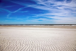 A beach with sand ripples and a clear blue sky.