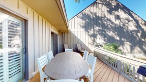 Un patio techado con una mesa redonda y sillas, una puerta corrediza de vidrio y una valla de madera.