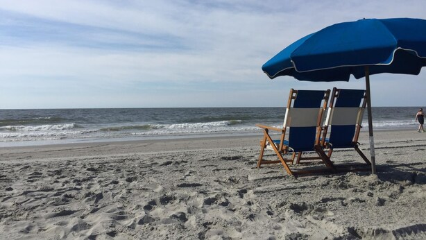 Une scène de plage avec un parasol bleu et une chaise de plage.