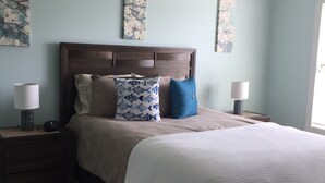 Une chambre à coucher avec un lit, une tête de lit en bois, deux tables de chevet avec des lampes et des œuvres d’art accrochées aux murs.