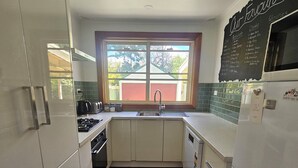 A compact kitchen with white cabinets, a wooden floor, a window with a view, and a chalkboard menu. - 3 bed 2 bath central cottage (Orange)