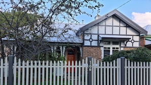 A traditional house with a white picket fence, a brick chimney, and a red door. - 3 bed 2 bath central cottage (Orange)