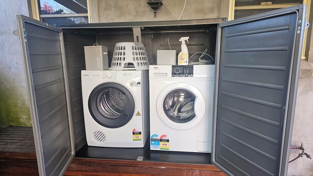 A compact laundry room with two washing machines, a basket, and a spray bottle. - 3 bed 2 bath central cottage (Orange)