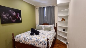 A bedroom with a wooden bed, a green wall, a painting, and a white shelf unit. - 3 bed 2 bath central cottage (Orange)