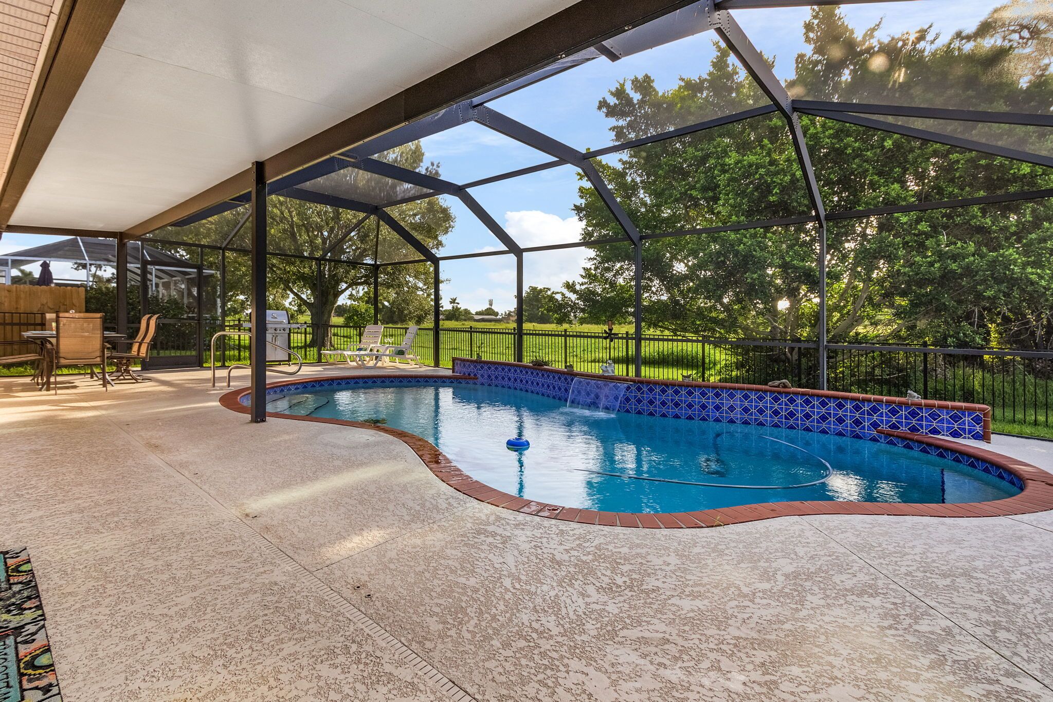Une piscine extérieure couverte, bordée de carreaux, entourée d’une clôture, et un espace patio aménagé avec du mobilier d’extérieur.