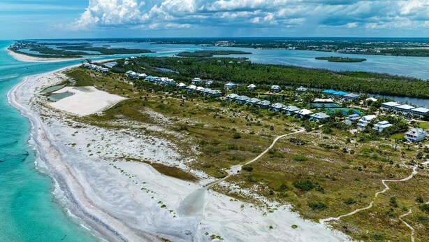 Vista aérea de un complejo turístico costero con propiedades frente al mar, una playa de arena y una vista despejada del agua y las islas circundantes.