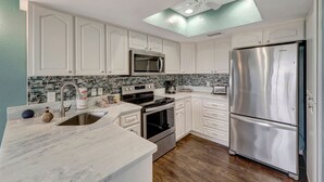 Una cocina moderna con armarios blancos, electrodomésticos de acero inoxidable, encimera de mármol y techo con tragaluces.