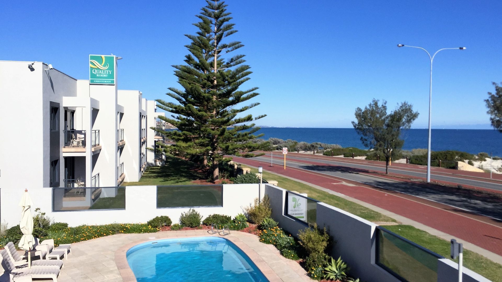 A modern building with a pool, a sign for 'Quality Resorts', and a view of the sea.