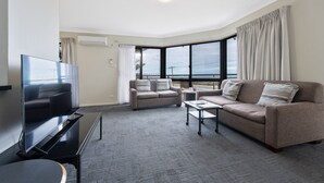 A modern living room with a flat-screen TV, two sofas, a coffee table, and a large window with curtains.