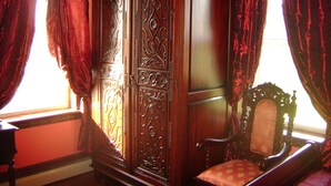 A room with a large wooden wardrobe, a chair with a patterned cushion, and red curtains. - Room #1 We are only 30 min. away from  "BASEBALL HALL OF FAME" in Coopers Town . (Fort Plain)