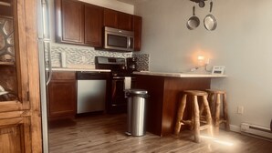 A modern kitchen with wooden cabinets, stainless steel appliances, and a small bar area with stools.