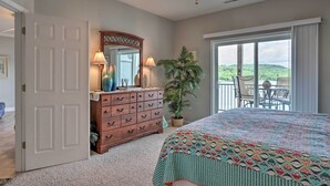 Une chambre avec un grand lit, une commode, un miroir, un ventilateur de plafond et une vue sur un balcon équipé de chaises.