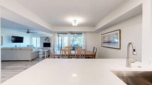 A modern living room with a sofa, TV, and ceiling fan. There is a dining area with a table and chairs.
