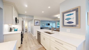 A modern kitchen with white cabinetry, a sink, and a countertop. There is a dining area with a table and chairs visible in the background. - Many Updates in this Large Four Bedroom Villa with Golf Views! (Hilton Head)