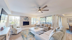 A spacious living room with a fireplace, comfortable seating, and large windows offering a view of the outdoors. - Many Updates in this Large Four Bedroom Villa with Golf Views! (Hilton Head)