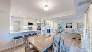 A modern kitchen with white cabinets, a central island, and a dining area with wooden chairs and a table. - Many Updates in this Large Four Bedroom Villa with Golf Views! (Hilton Head)