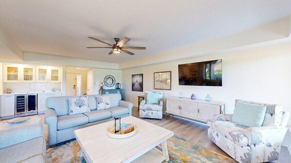 A spacious living room with a light blue sofa, a patterned armchair, a white coffee table, and a ceiling fan.