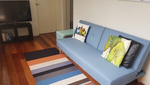 Uma sala de estar com um sofá azul, tapete listrado colorido e uma televisão de tela plana em um suporte.