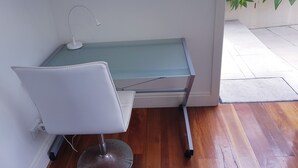 Escritório de canto com cadeira branca, mesa de vidro e uma pequena mesa.