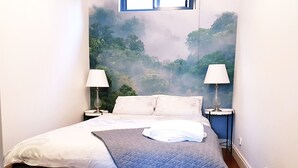 Uma cama bem arrumada com um edredom acolchoado, duas luminárias de cabeceira e um mural na parede com uma cena de floresta.