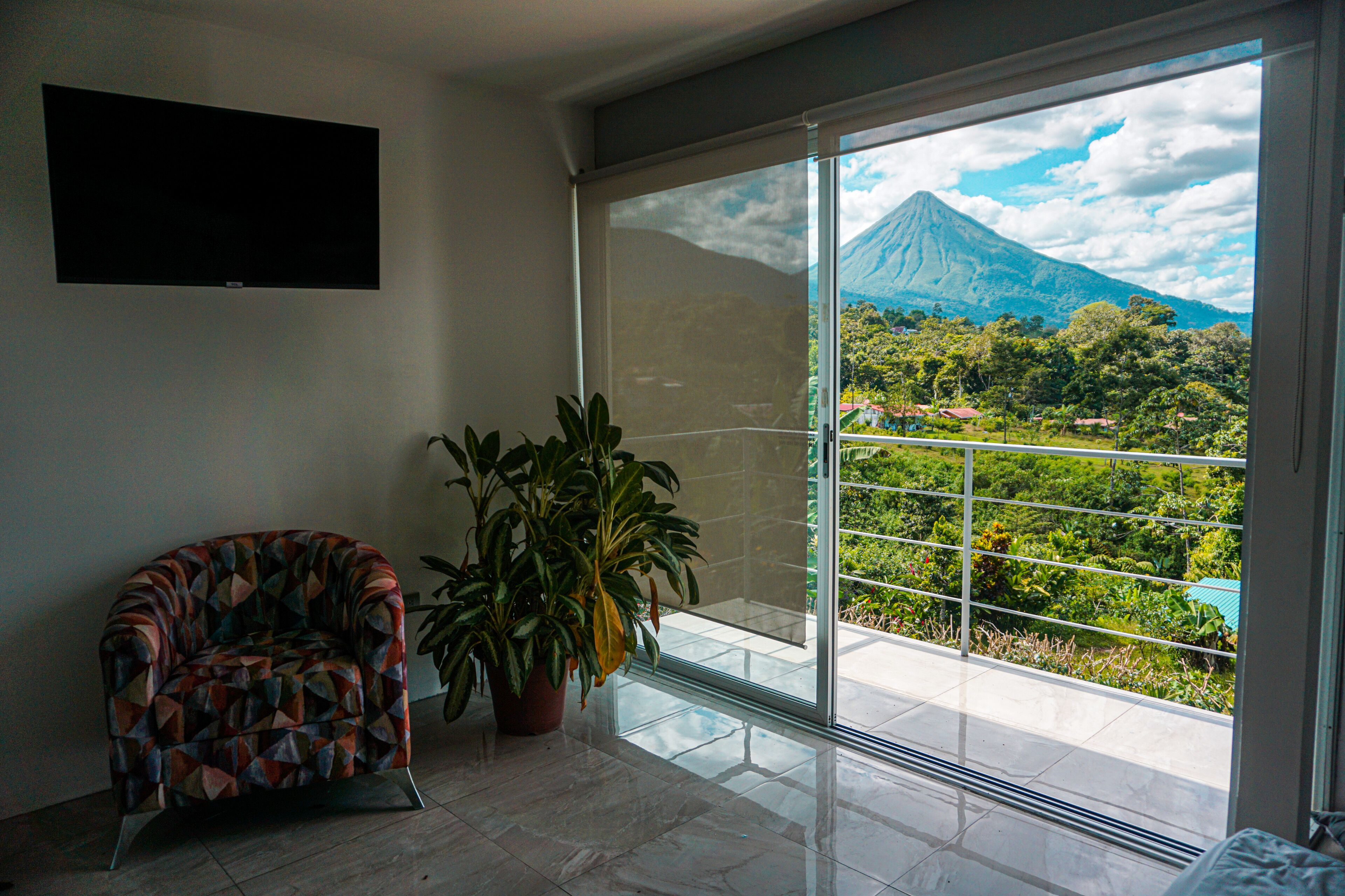 Una habitación con un gran ventanal corredero que da a un balcón con vistas a una montaña.