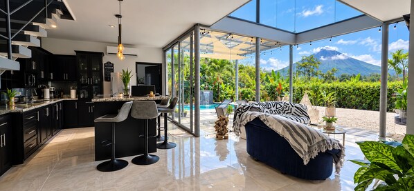 A modern kitchen with a bar area, a dining space with a view of a mountain, and a cozy seating area with a view of lush greenery.