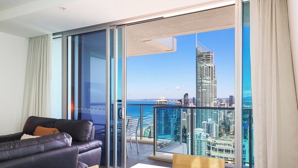 Une chambre d’hôtel moderne avec balcon, un canapé en cuir, une table à manger et une vue sur la ville.