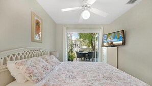 Une chambre à coucher avec un lit, un ventilateur de plafond, une télévision et une vue sur l’extérieur.